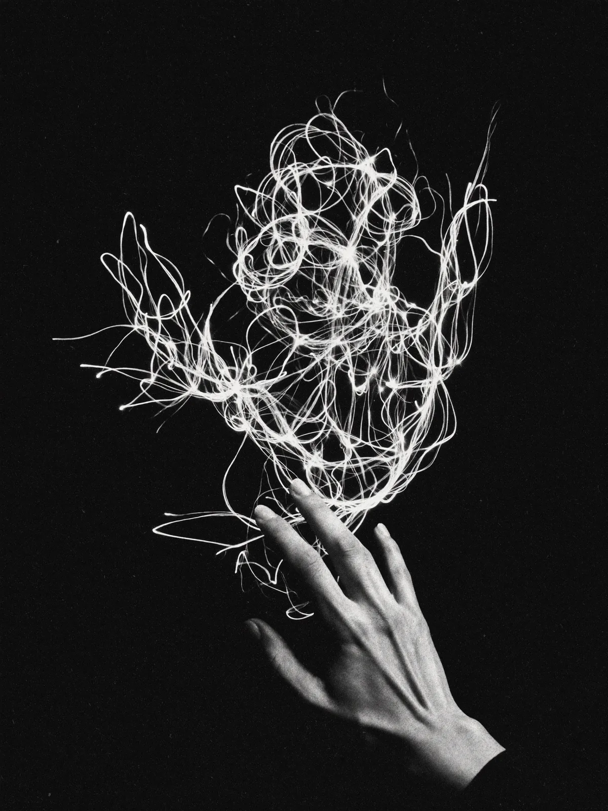 Main touchant des filaments de lumière dans l'obscurité, noir et blanc