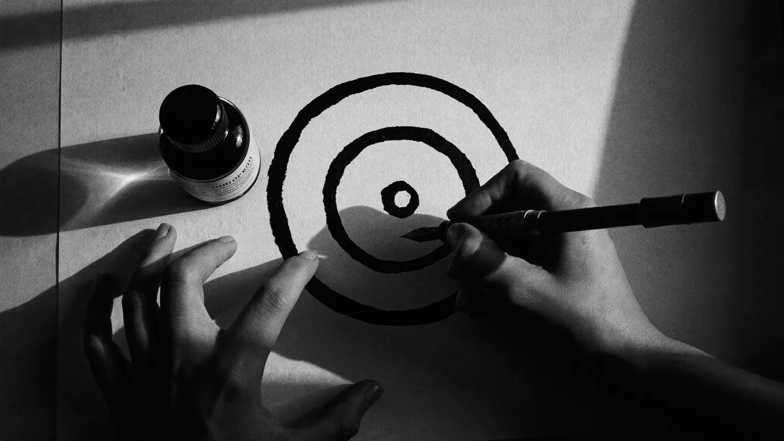 Mains traçant une spirale à l'encre sur papier, noir et blanc